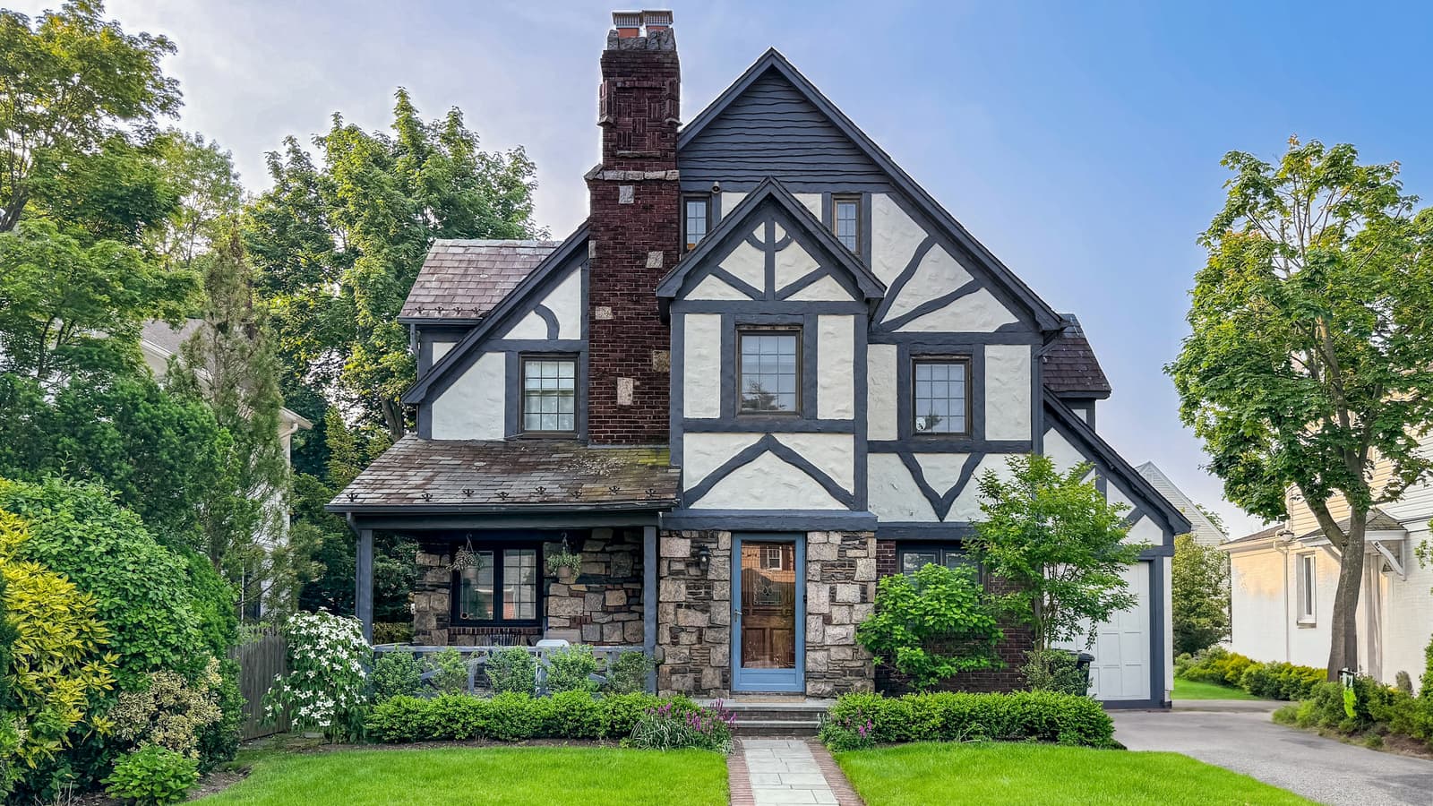 Tudor-style two-story home with stone accents, a dark asphalt-shingle roof and a neatly trimmed green front lawn